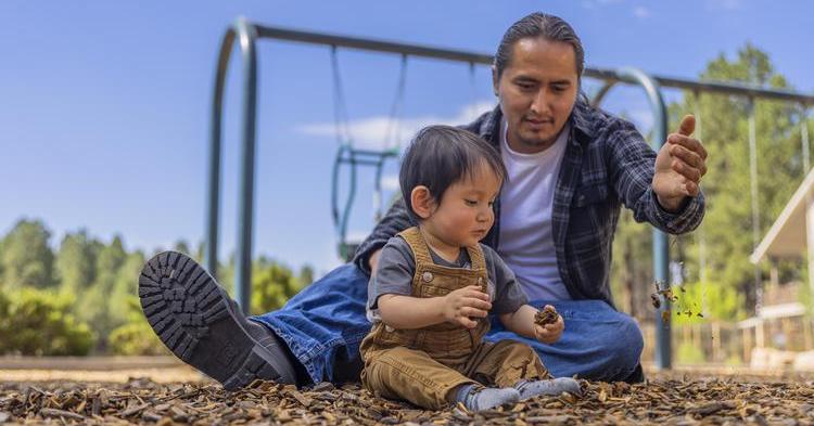 Father sitting in park and playing with toddler boy