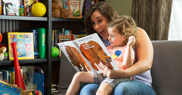 Mother reading a book to her little girl. The girl is in her mother's lap.